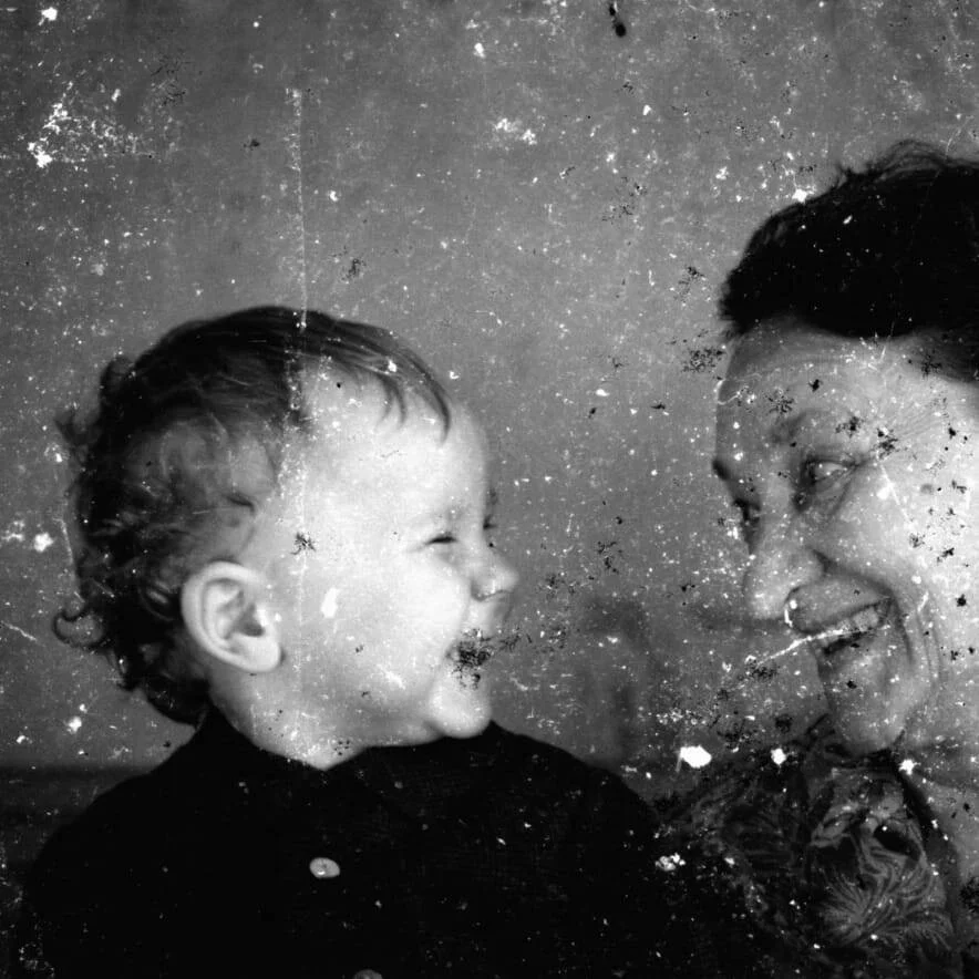 Foto en blanco y negro deteriorada de un bebé y un adulto sonriendo juntos.