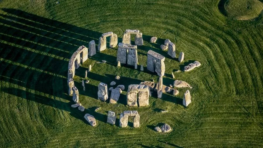 Vista aérea de Stonehenge mostrando el círculo de megalitos prehistóricos sobre una llanura verde con largas sombras al atardecer.