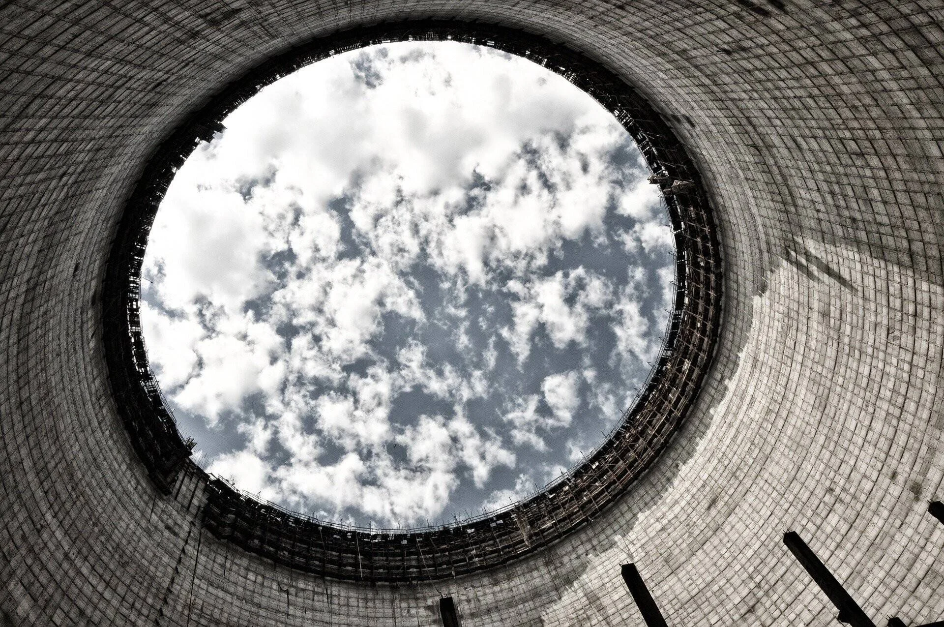 Vista desde el interior de una torre de enfriamiento de hormigón hacia el cielo nublado, enmarcado por la abertura circular en la cima.
