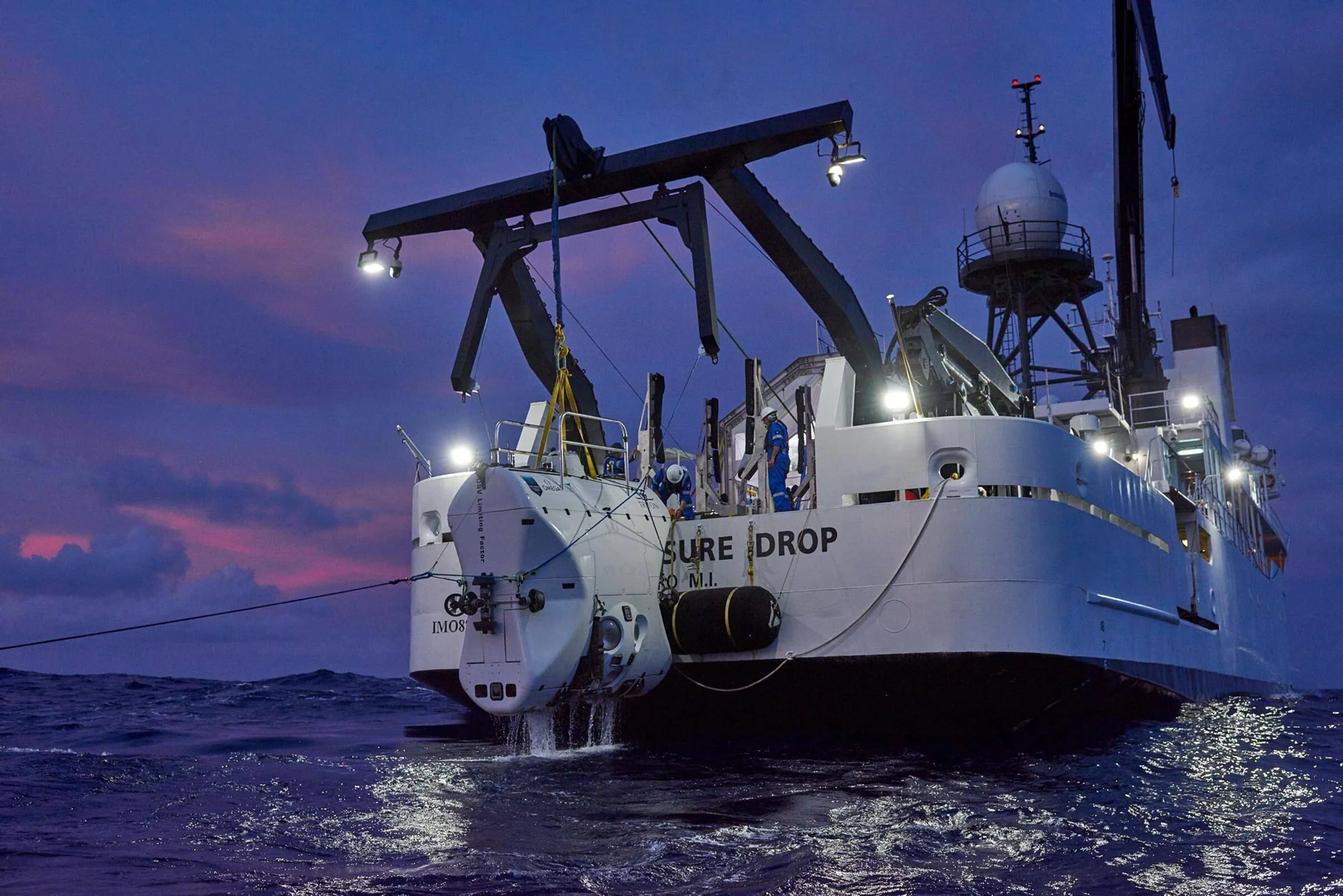 Submarino de exploración profunda siendo desplegado desde el buque 'Pressure Drop' al anochecer en alta mar.