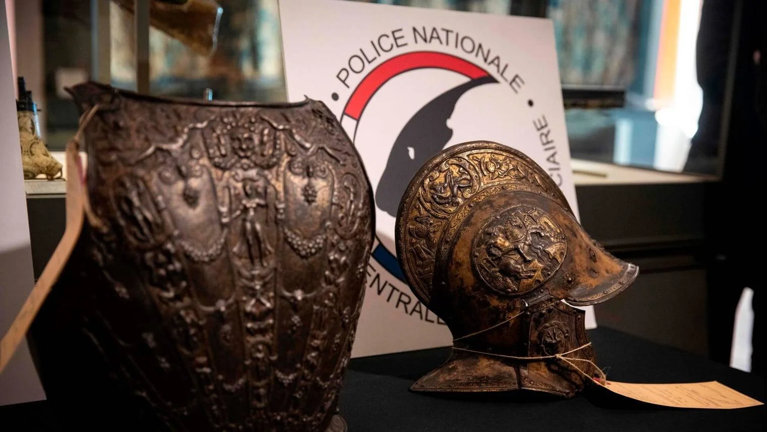 Piezas de armadura medieval grabada —coraza y yelmo— exhibidas ante el logo de la Police Nationale francesa tras su recuperación.