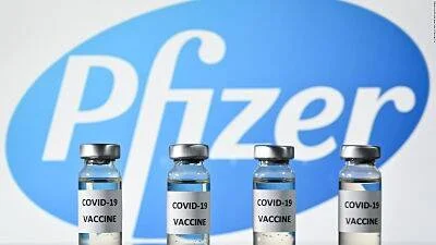 Cuatro viales de vacuna contra COVID-19 frente al logotipo de Pfizer en fondo azul.