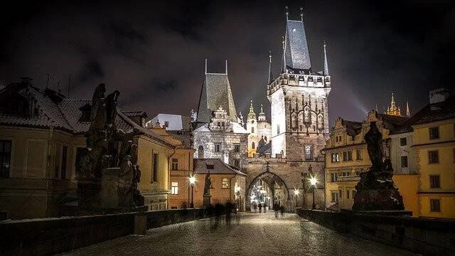 Vista nocturna del Puente de Carlos en Praga con sus torres góticas iluminadas y estatuas a los lados.