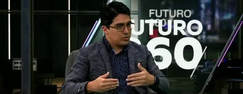 Hombre con lentes y saco gris gesticula mientras habla en el programa de televisión Futuro 360.
