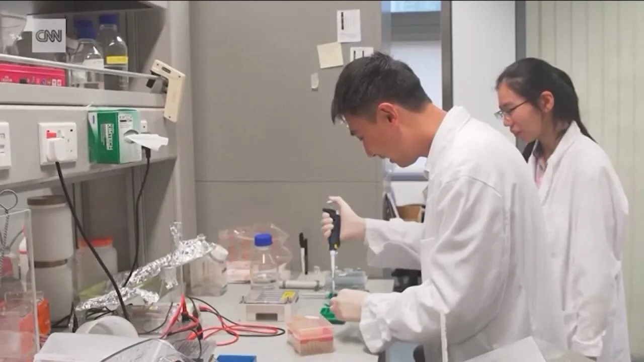 Dos investigadores con batas blancas manipulan muestras con una pipeta en una mesa de laboratorio equipada con reactivos y materiales de análisis.