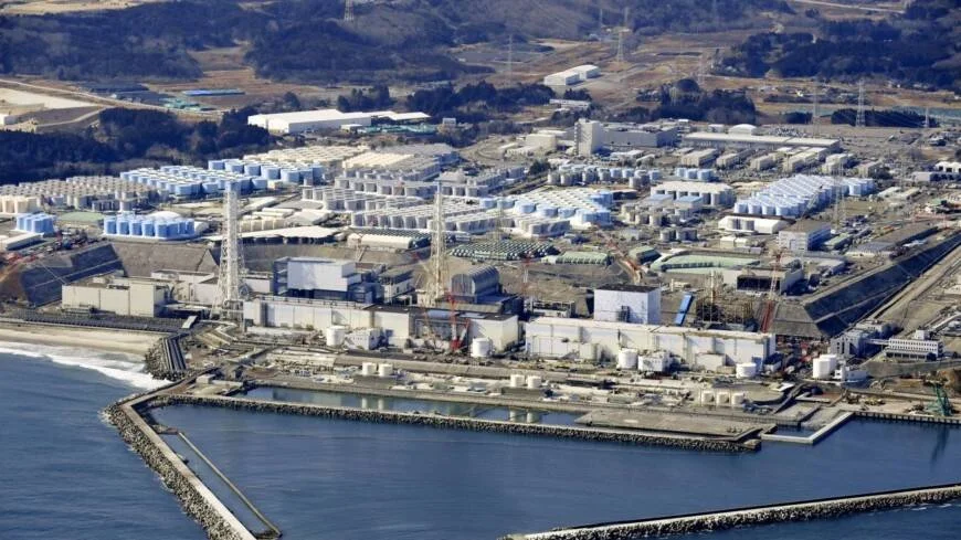Vista aérea de una central nuclear costera rodeada de cientos de tanques de almacenamiento de agua, junto al océano.