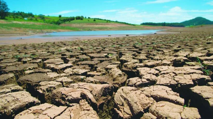 Tierra reseca y agrietada en el lecho de un embalse con escaso nivel de agua al fondo, evidenciando una severa sequía.