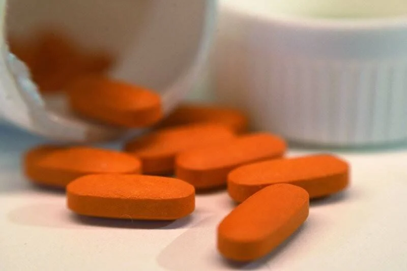 Varias pastillas de color naranja derramadas fuera de un frasco blanco de medicamento.