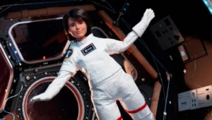 Muñeca Barbie vestida con traje espacial blanco de la ESA, flotando dentro de una estación espacial en microgravedad.