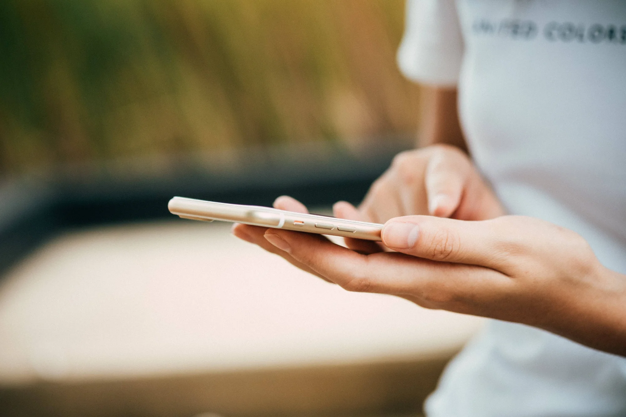 Persona sosteniendo un teléfono inteligente dorado con ambas manos al aire libre.