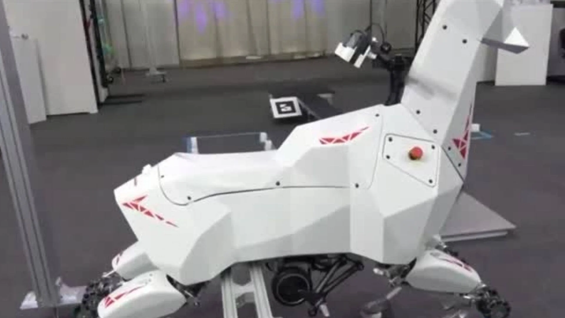 Robot cuadrúpedo de carcasa blanca con marcas rojas y forma animal poligonal expuesto en sala de exhibición.