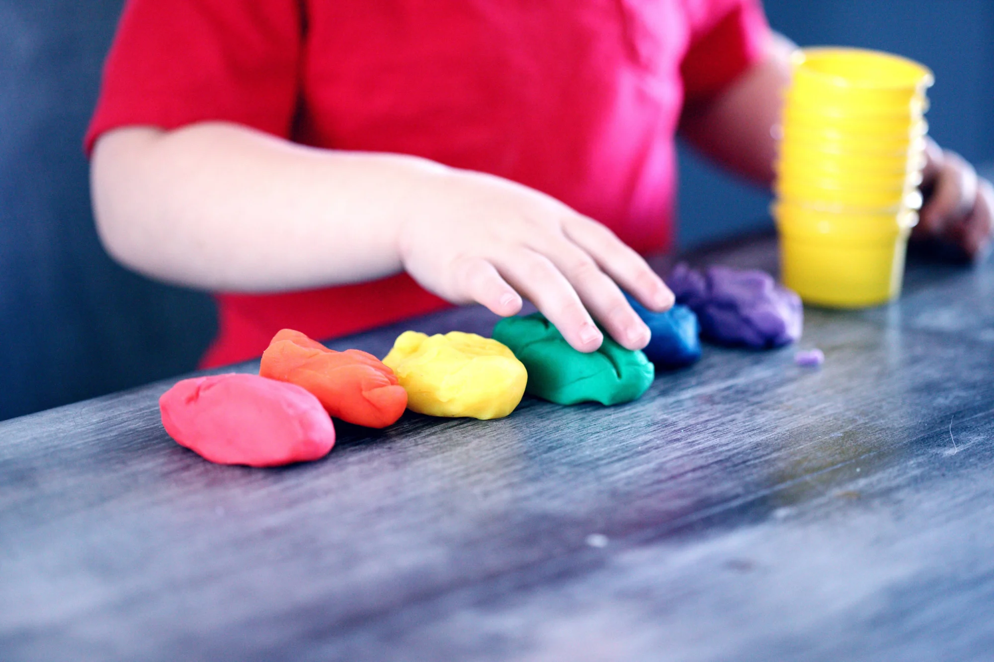 Un niño con remera roja alinea trozos de plastilina de distintos colores sobre una mesa.