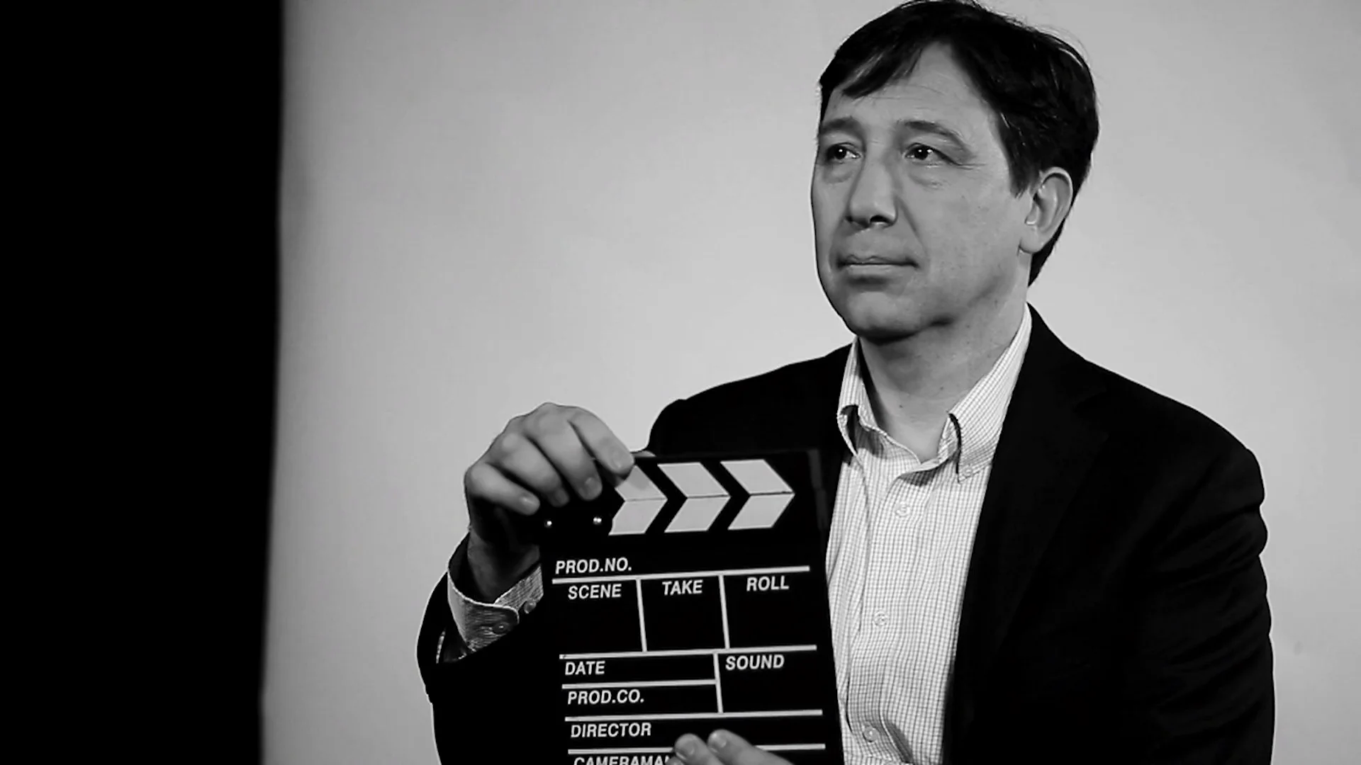 Hombre con traje sostiene una claqueta de filmación en una foto en blanco y negro.