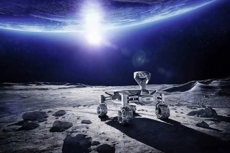 Rover robótico con logo de Audi sobre la superficie lunar, con la Tierra iluminada al fondo en el espacio.