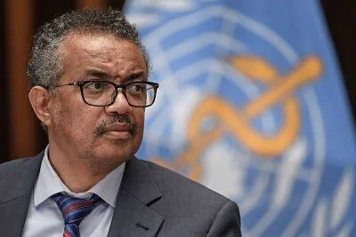 Hombre con traje y corbata frente al emblema azul de la Organización Mundial de la Salud.
