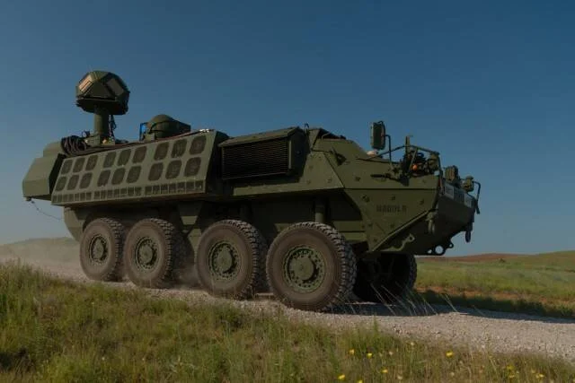 Vehículo blindado de ruedas Stryker equipado con sistema de arma láser avanza por camino de tierra en terreno abierto.