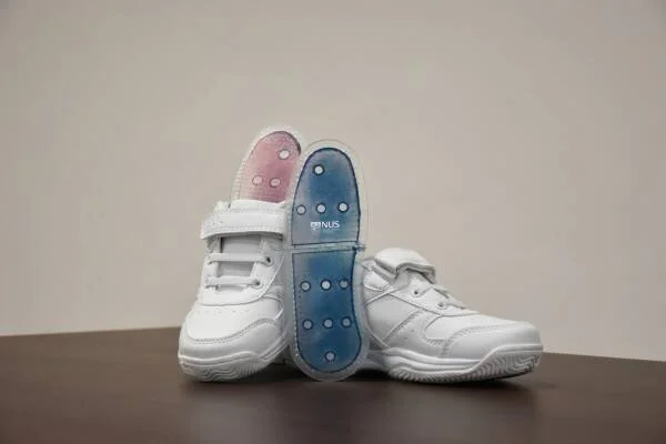 Par de zapatillas blancas para niños con velcro, junto a una plantilla bicolor azul y rosa con sensores desarrollada por NUS.