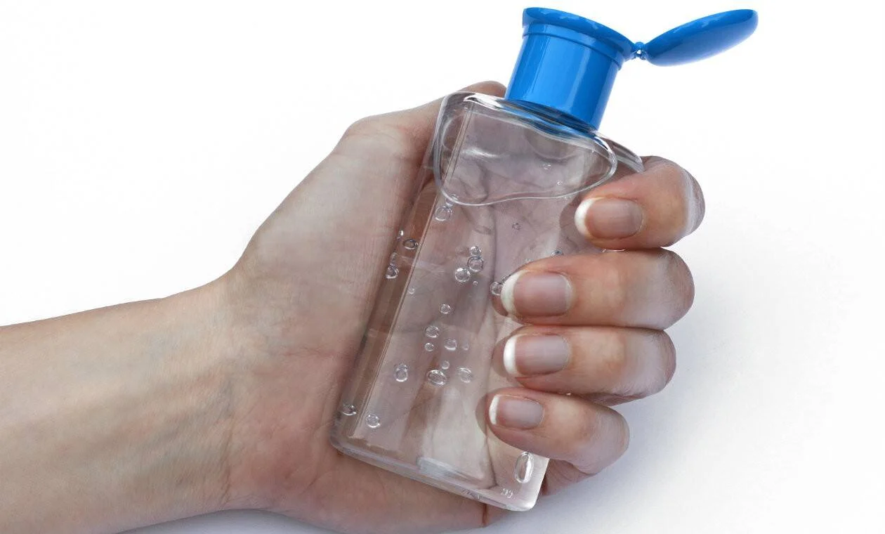 Una mano sujeta con fuerza un frasco transparente de gel desinfectante con tapa azul abierta.
