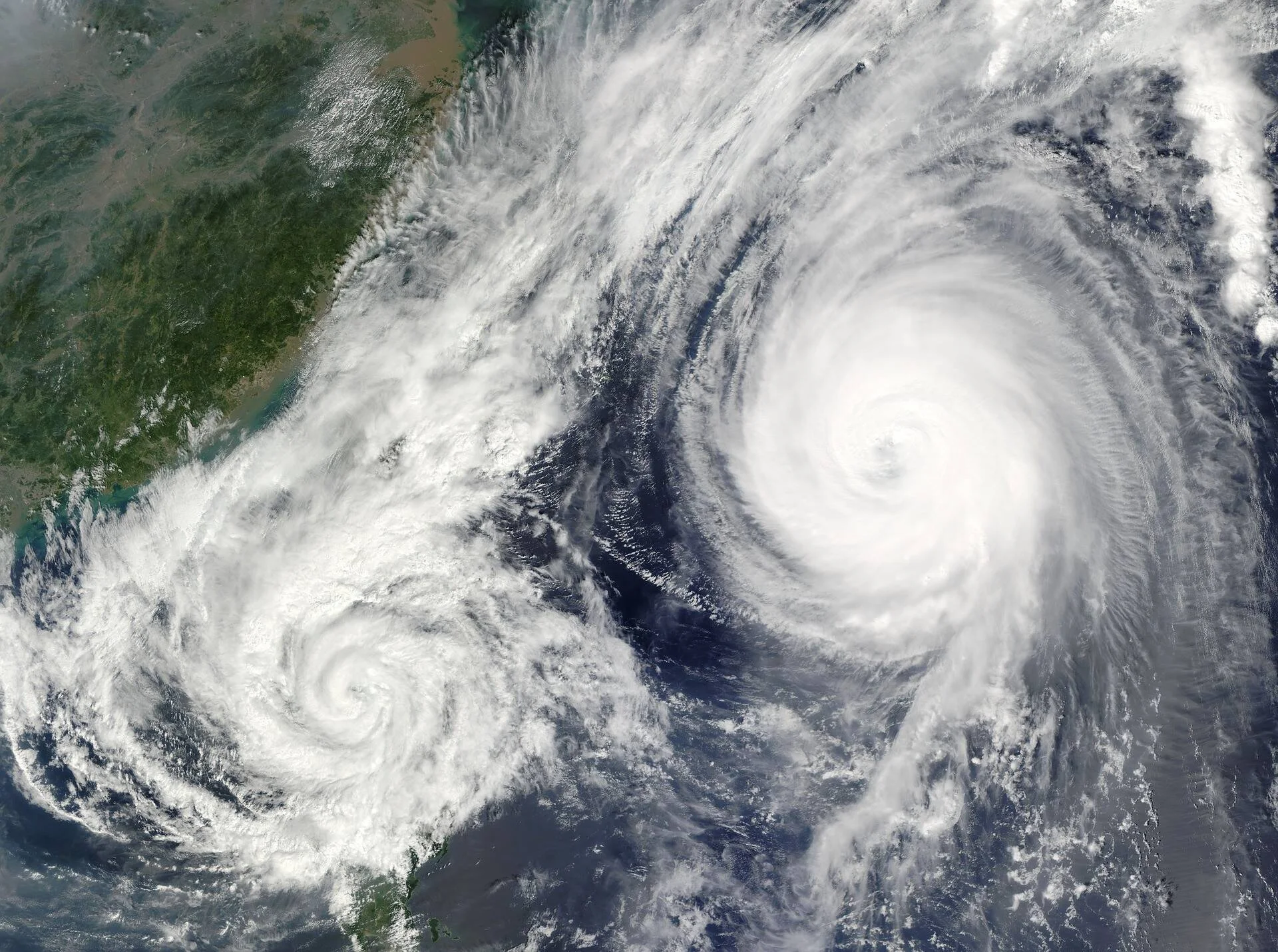 Vista satelital de dos ciclones tropicales con ojo bien definido aproximándose a una costa continental.