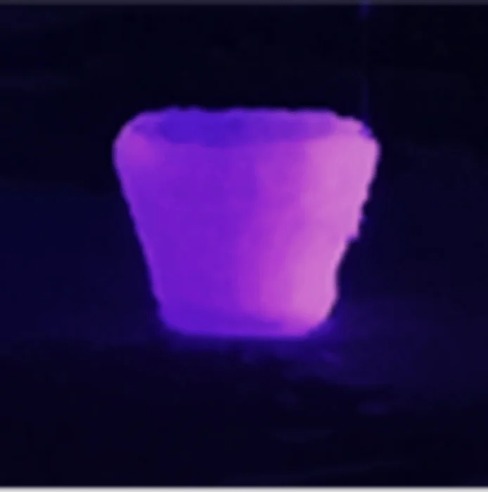 Recipiente en forma de vaso que emite fluorescencia violeta-rosa bajo luz ultravioleta en ambiente oscuro.