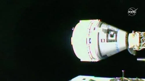 Cápsula espacial Boeing Starliner vista desde la Estación Espacial Internacional, con el logo de la NASA visible en la esquina superior derecha.