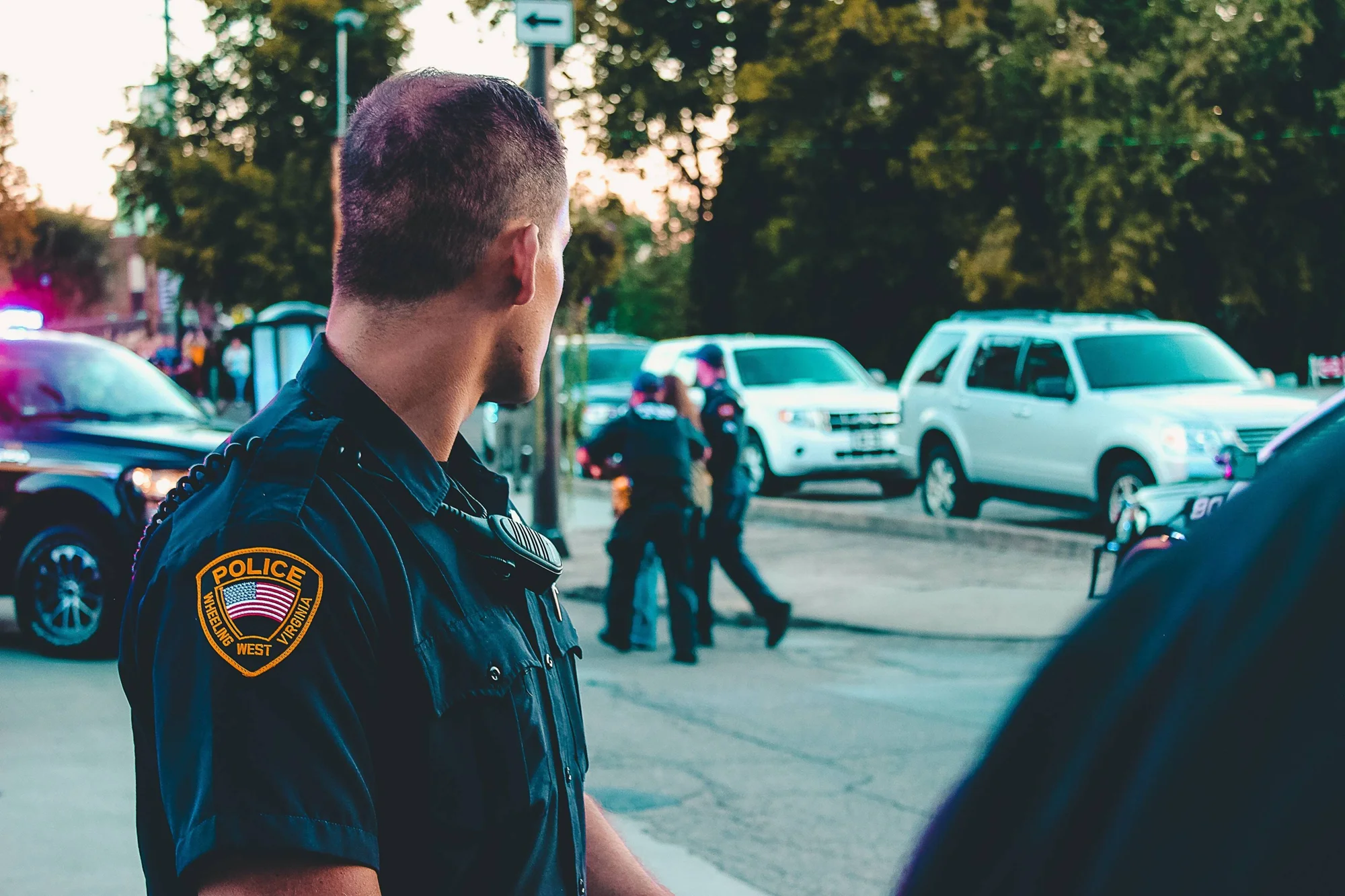 Oficial de policía de Wheeling, West Virginia, observa un operativo policial en la calle con vehículos y compañeros al fondo.