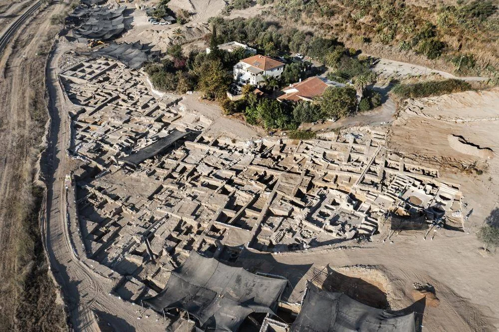 Vista aérea de un extenso sitio arqueológico con estructuras de piedra excavadas y una vivienda moderna al fondo.