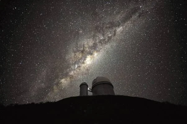 Cúpulas de un observatorio astronómico en lo alto de una colina, con la Vía Láctea iluminando el cielo estrellado.