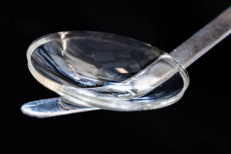 Lente intraocular de silicona transparente sostenida por un aplicador, vista en detalle sobre fondo negro.