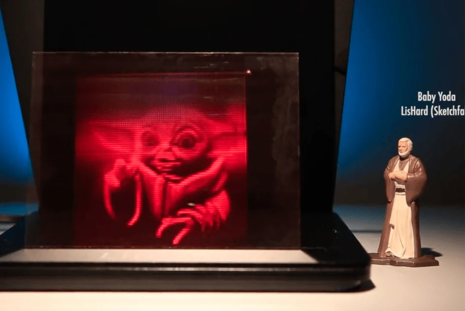 Holograma en rojo de Baby Yoda en una pantalla volumétrica, junto a una pequeña figura de un personaje de Star Wars.