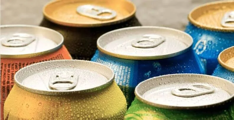 Varias latas de bebidas de distintos colores cubiertas de gotas de condensación, vistas desde arriba en primer plano.