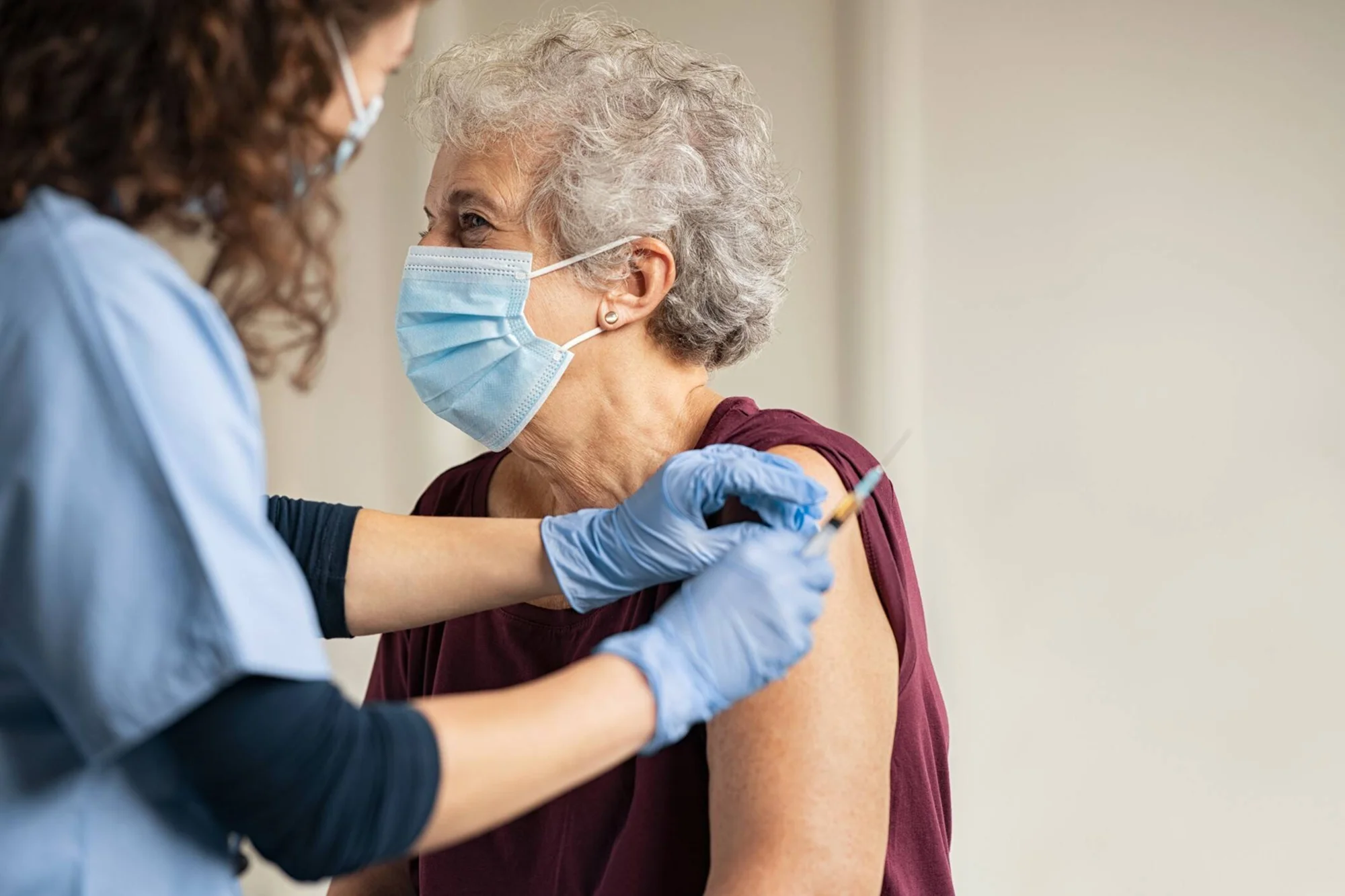 Profesional de salud con guantes aplica una inyección en el brazo de una mujer mayor con tapabocas.