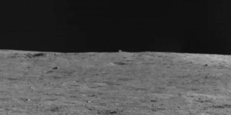 Fotografía en blanco y negro de la superficie lunar con un pequeño objeto cúbico visible en el horizonte.