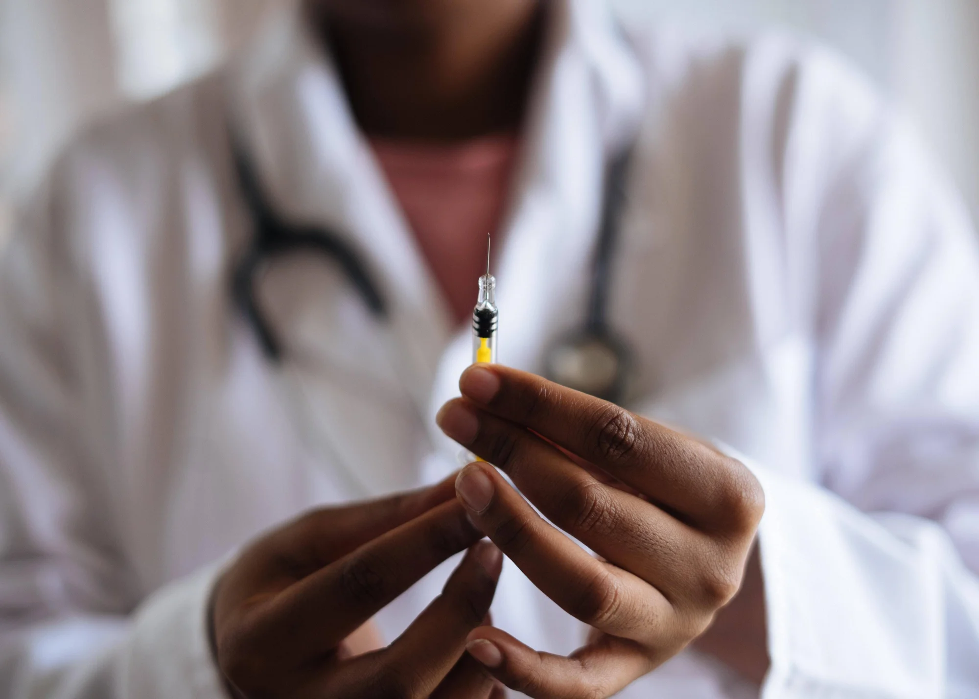 Profesional de la salud con guardapolvo blanco y estetoscopio sostiene una jeringa lista para aplicar una inyección.