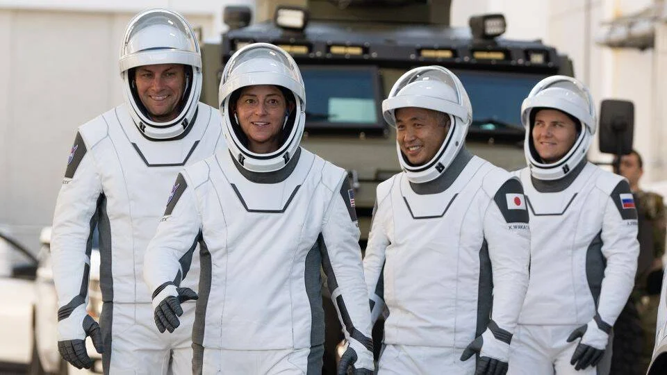 Cuatro astronautas con trajes blancos de SpaceX caminan juntos antes de un lanzamiento, incluyendo representantes de EE.UU., Japón y Rusia.