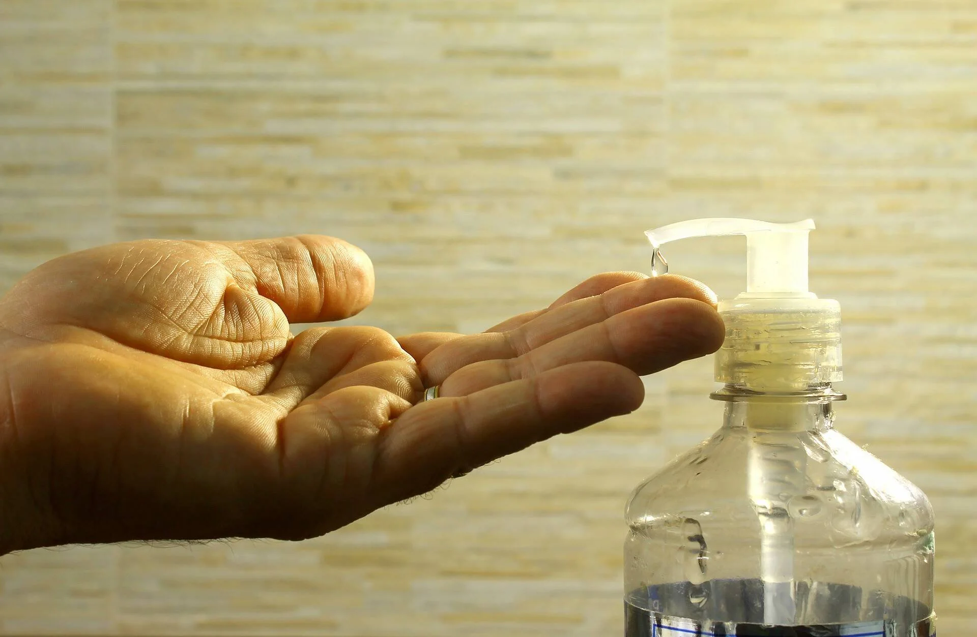 Una mano abierta recibe gel desinfectante dispensado desde una botella con bomba.