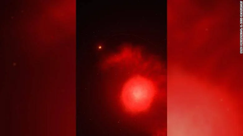 Fotografía astronómica que muestra una intensa esfera de luz roja con nubes luminosas captada desde un observatorio.