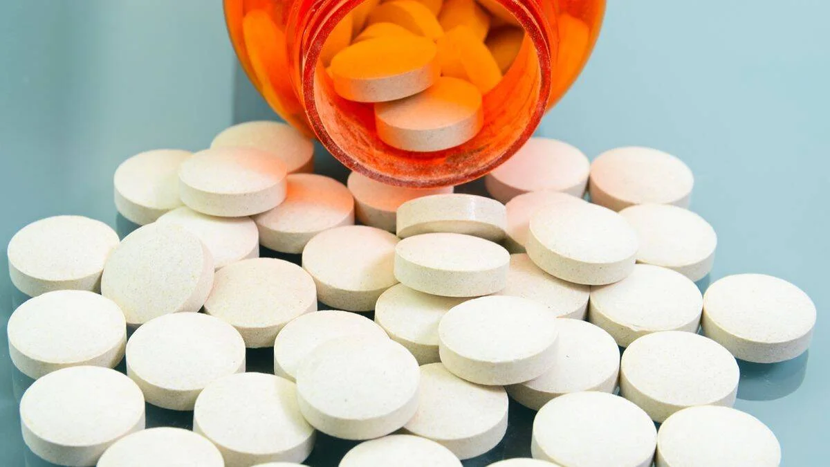 Numerosas pastillas blancas derramadas sobre una superficie desde un frasco de medicamento naranja volcado.