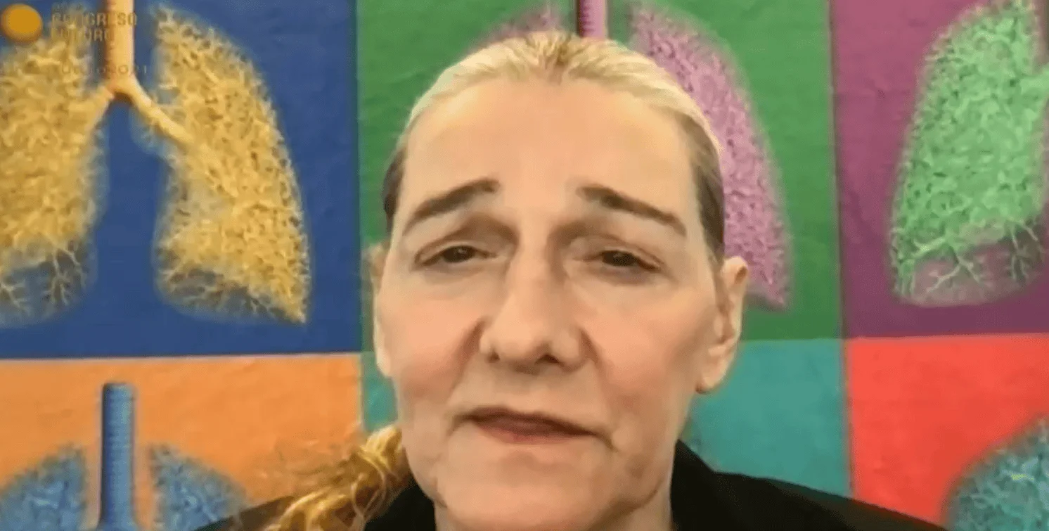Mujer adulta habla a cámara durante una videoconferencia de un congreso médico, con ilustraciones anatómicas de pulmones al fondo.