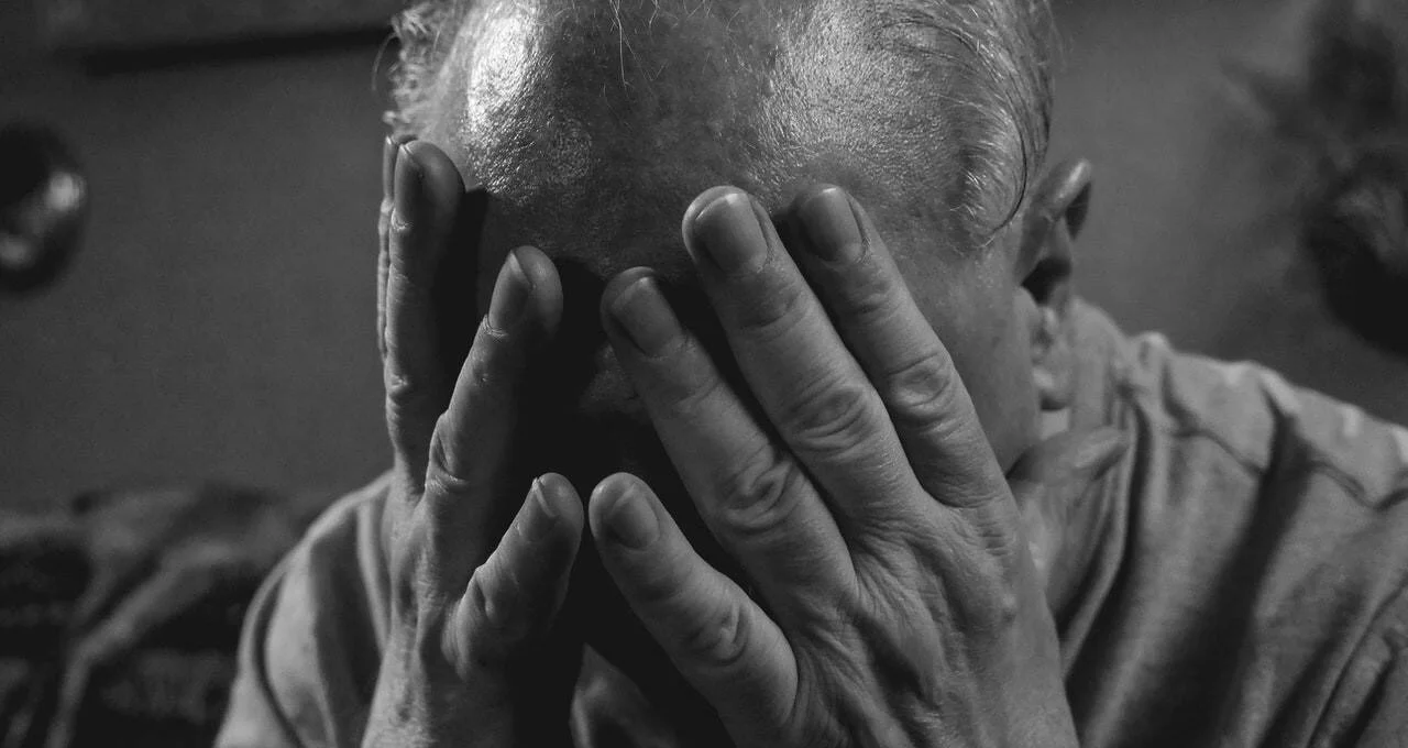Hombre mayor se cubre el rostro con ambas manos en un gesto de angustia o desesperación.