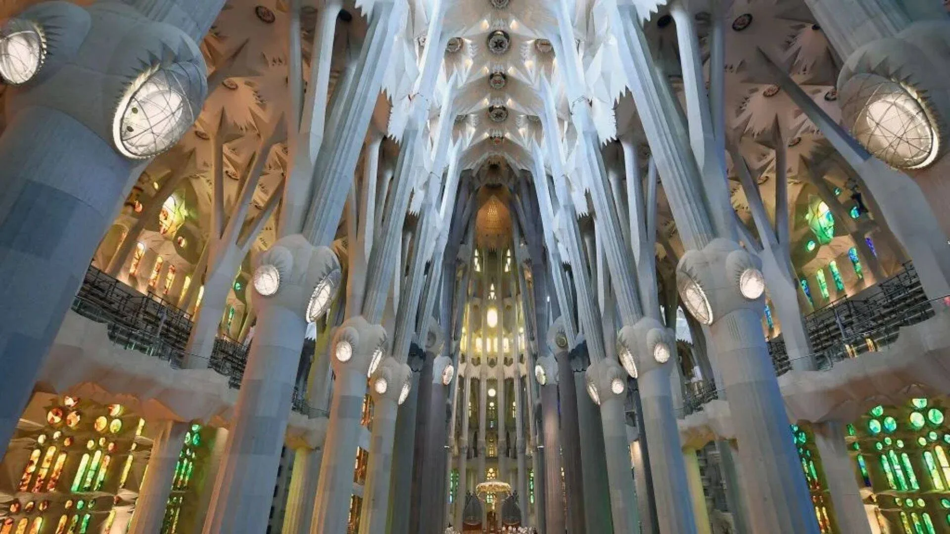 Nave central de la Sagrada Família con columnas arbóreas ramificadas, bóvedas blancas y vitrales de colores iluminando el espacio.
