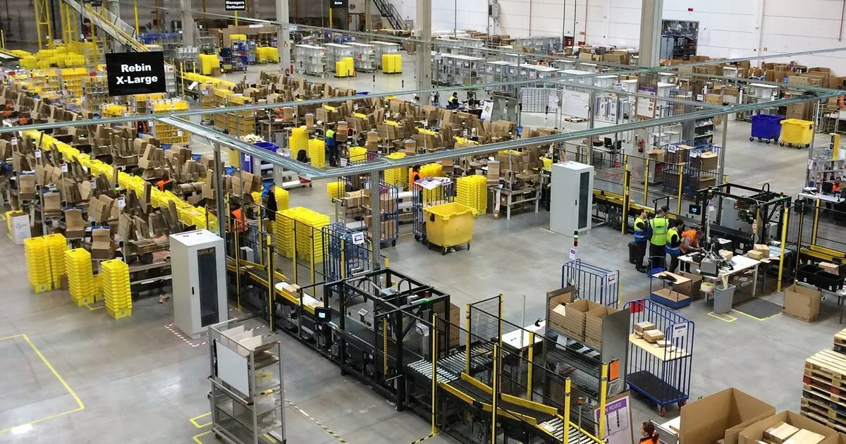 Vista aérea de un gran centro logístico con cintas transportadoras, cajas y trabajadores con chalecos de seguridad clasificando paquetes.