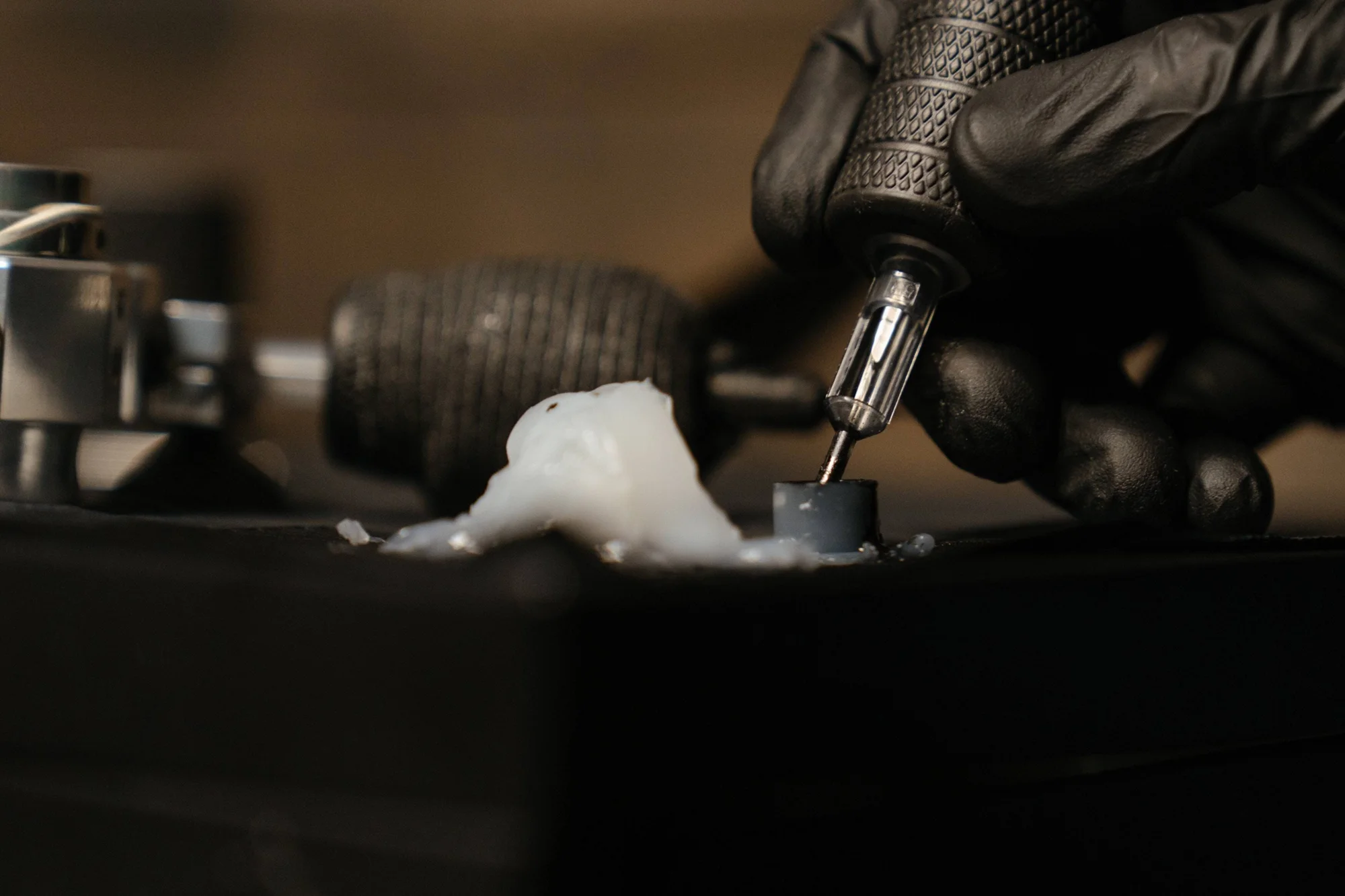 Mano enguantada en negro aprieta un tornillo pequeño con un destornillador de precisión sobre una superficie oscura con material blanco.