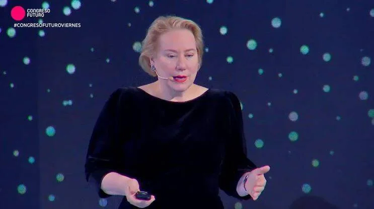 Oradora con micrófono de diadema presenta en el escenario del Congreso Futuro, con fondo oscuro y luces de colores.
