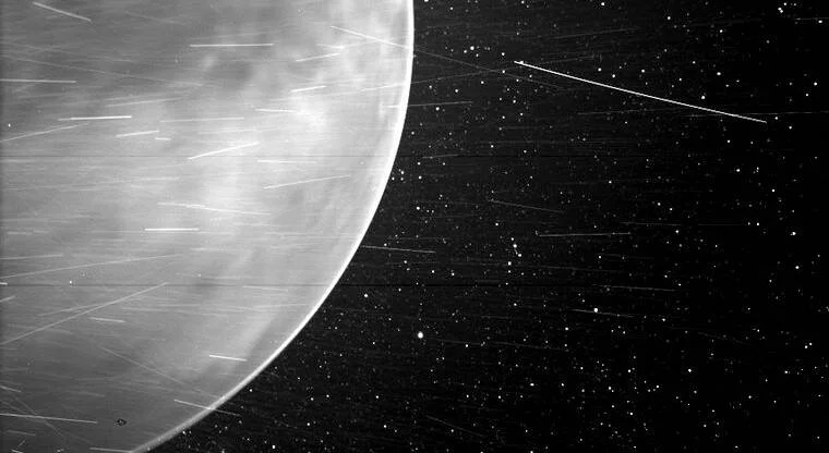 Vista en blanco y negro de Venus captada desde el espacio, con su atmósfera visible y estrellas al fondo.