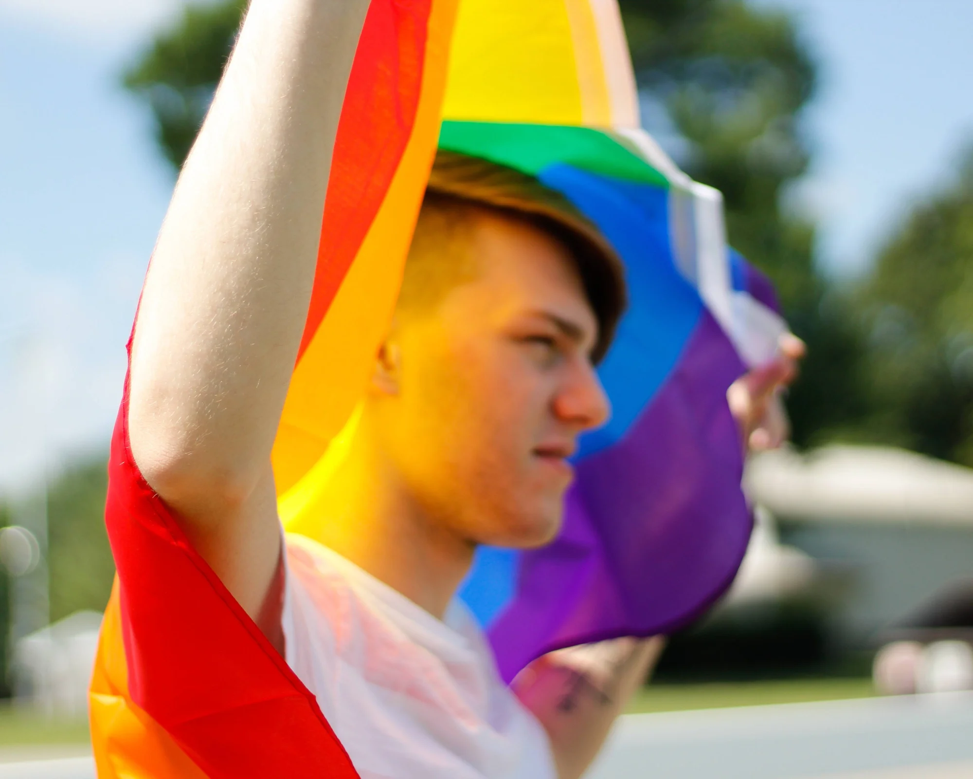 Joven levanta una bandera arcoíris del orgullo LGBT con el brazo en alto al aire libre.