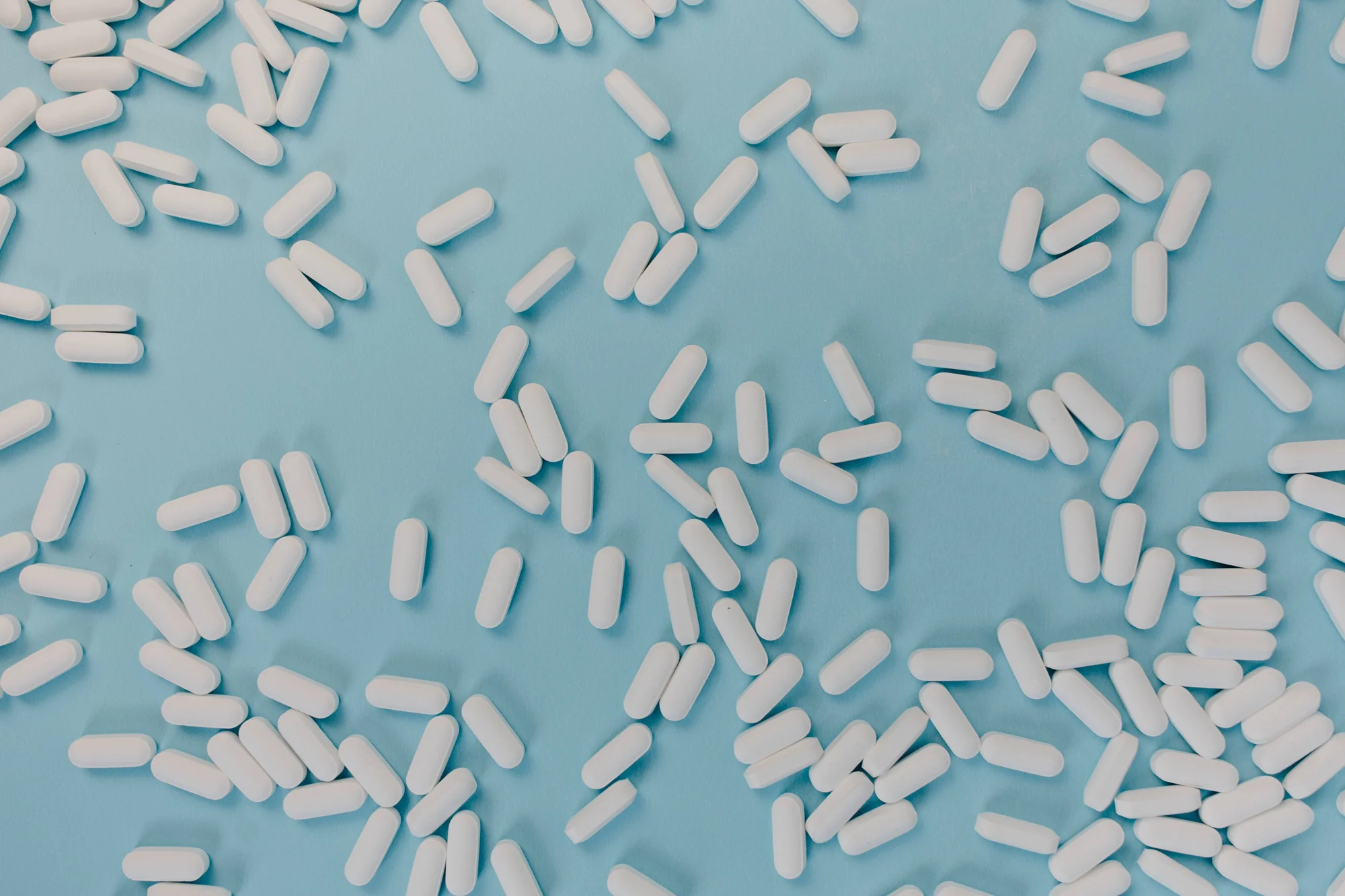 Numerosas pastillas o comprimidos blancos esparcidos sobre una superficie azul clara.