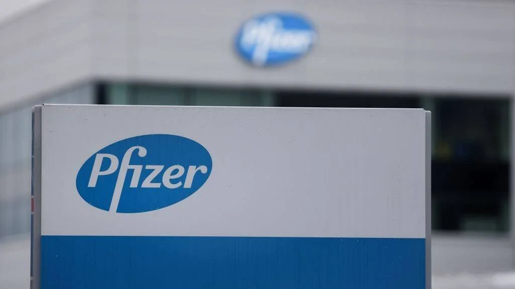 Cartel con el logotipo de Pfizer en primer plano y el edificio corporativo de la empresa al fondo.